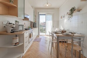 Cuina moderna amb armaris blancs, zona de menjador amb taula i cadires, i vista cap a l'exterior per una porta de vidre.
