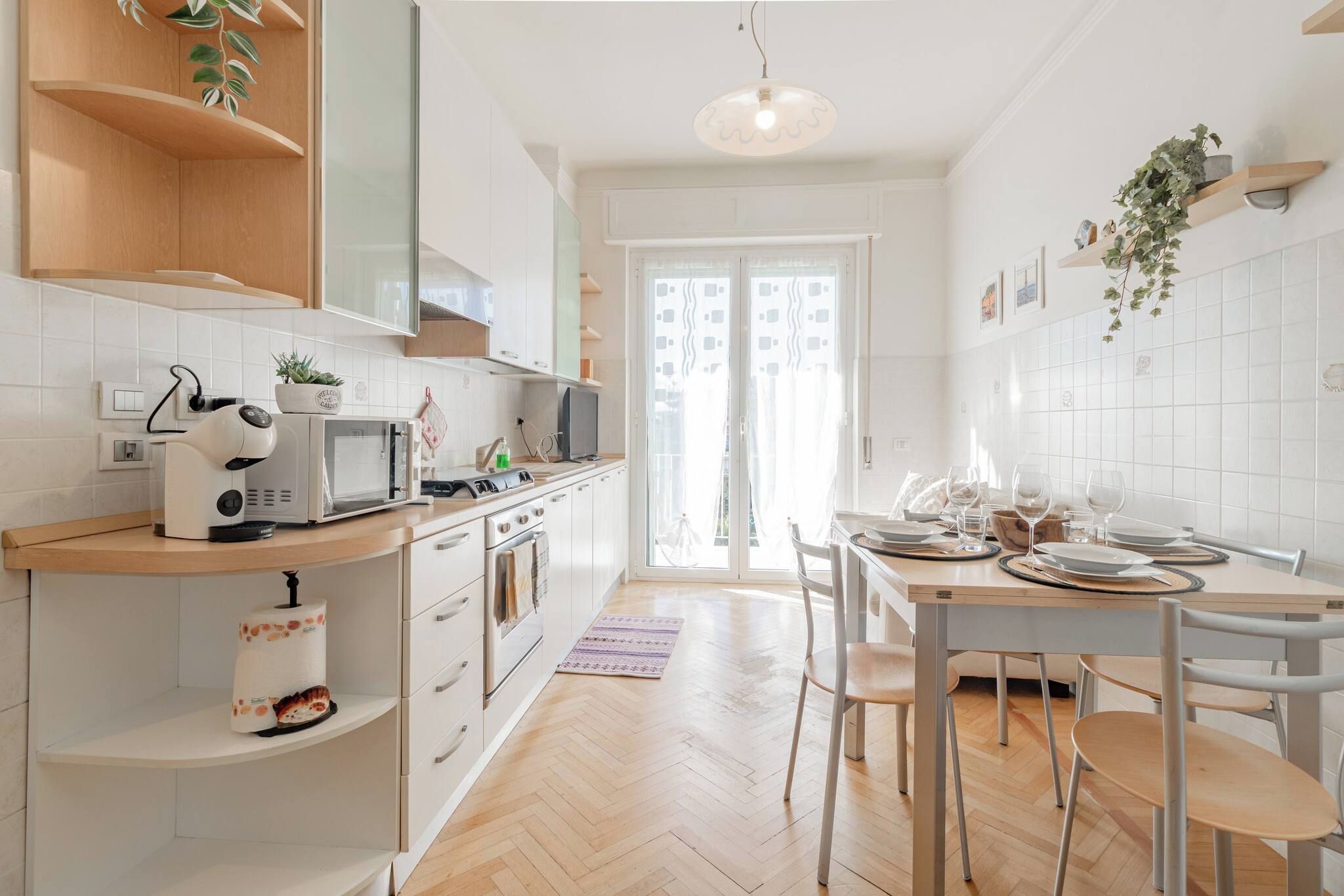 A modern kitchen with white cabinetry, a built-in oven, a microwave, and a dining area with a table and chairs.