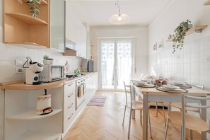 A modern kitchen with white cabinetry, a built-in oven, a microwave, and a dining area with a table and chairs. - CASA ARMONIA - Vista Mare - Sanremo (Sanremo)