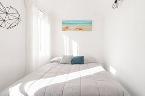 Ein Schlafzimmer mit einem Bett, zwei Kissen, einem Fenster mit Vorhängen, einem Wandbild und einer geometrischen Leuchte.