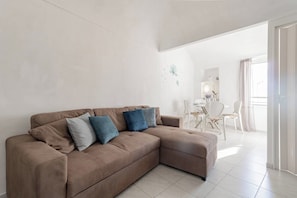 Un soggiorno moderno con un divano modulare beige, un'area pranzo con sedie bianche e un'ampia finestra che offre luce naturale.