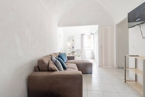 Ein modernes Wohnzimmer mit einer Eckcouch, einem an der Wand montierten Fernseher und einem Essbereich im Hintergrund.