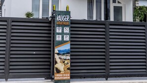 Ein modernes, zweistöckiges Gebäude mit einem Holzbalkon, einem schwarzen Tor und einem Schild, das KAUGER APARTMANNI bewirbt.