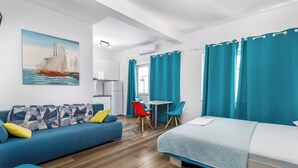 Ein modernes Hotelzimmer mit einem blauen Sofa, einem Bett, einem Esstisch mit Stühlen und einem Bild eines Segelboots.