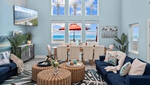 Ein Wohnzimmer mit großem Fenster zum Strand, einem Essbereich mit Tisch und Stühlen und einem blauen Sofa.