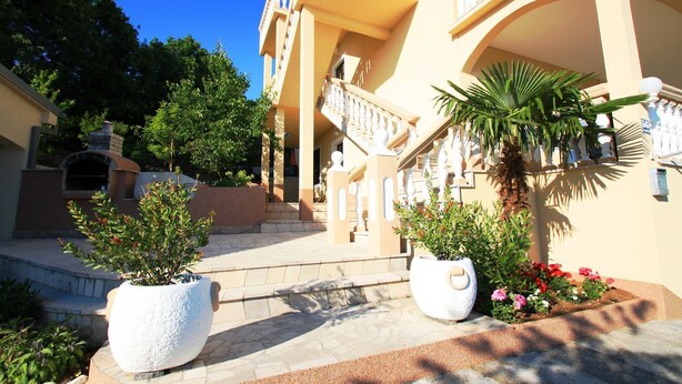 Un immeuble à plusieurs étages doté d’un escalier central, de plantes en pot disposées à l’extérieur et surplombant un ciel bleu dégagé.