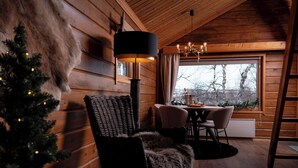 Interior acogedor de una cabaña con detalles de madera, un comedor, un árbol de Navidad y un ventanal grande.