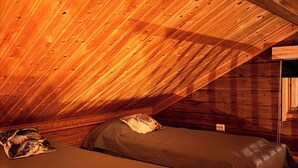 Acogedor dormitorio en ático con paredes de madera y techos inclinados, con dos camas con almohadas y una mesita de noche pequeña.