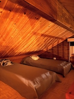 Um quarto de sótão aconchegante, com paredes de madeira e teto inclinado, com duas camas, almofadas e uma pequena mesa de cabeceira.