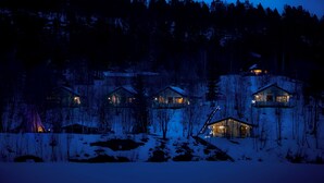 Un grupo de cabañas en un bosque nevado, de noche.