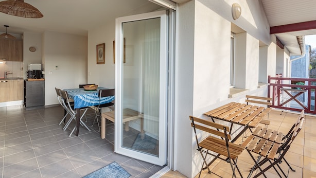 Une cuisine moderne dotée d’un four encastré, un coin repas avec une table et des chaises, et une porte-fenêtre coulissante donnant sur une terrasse extérieure aménagée avec du mobilier en bois.