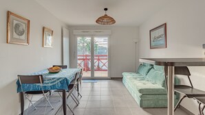 Un coin repas comprenant une table et des chaises, un canapé et, derrière une porte vitrée, une vue sur un espace extérieur doté d’une rambarde rouge.