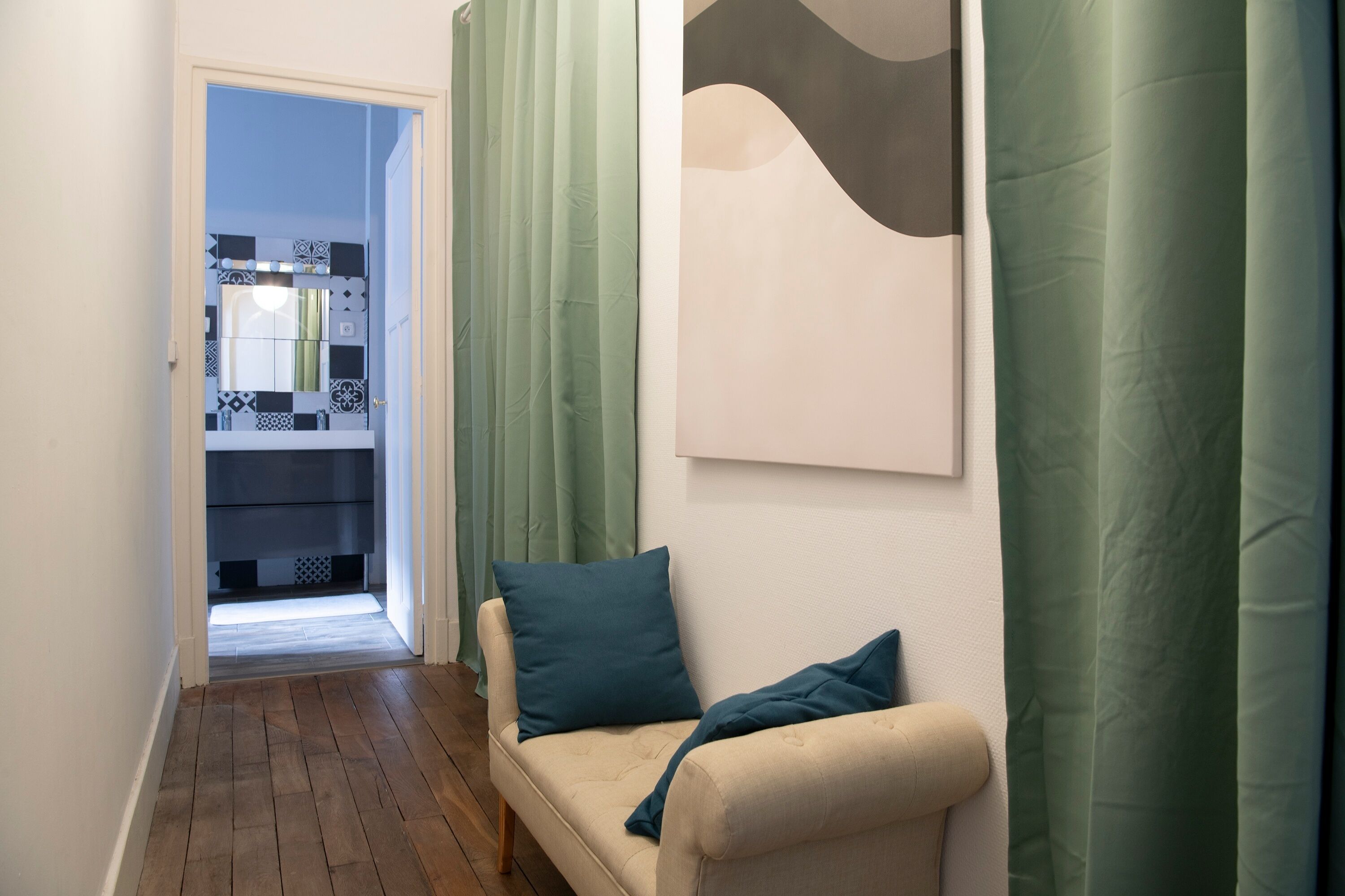 A hallway with a beige sofa, green curtains, and a modern abstract painting on the wall.