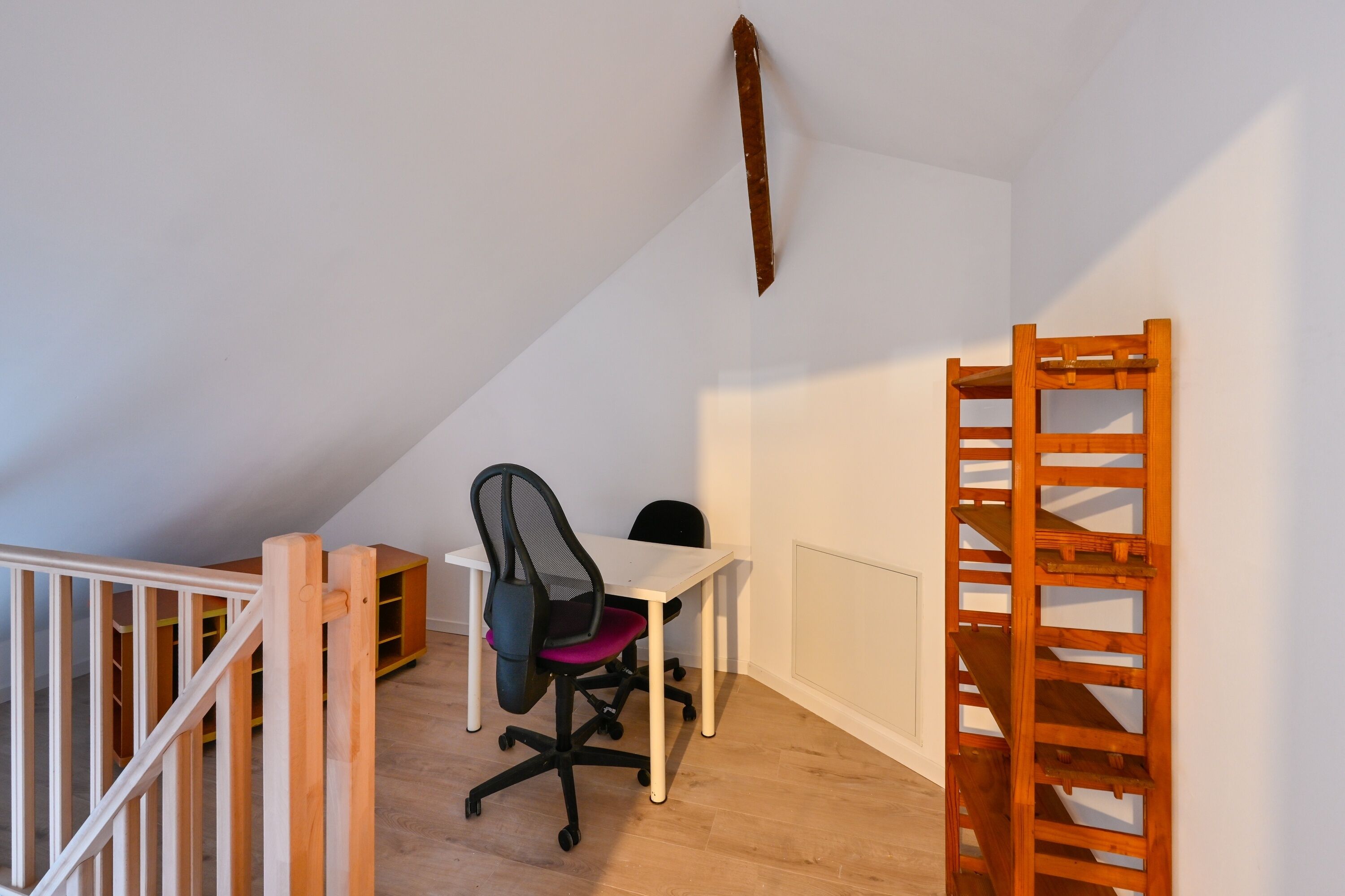 Une petite pièce bien éclairée, avec un bureau en bois, une chaise de bureau noire et une échelle en bois appuyée contre le mur.