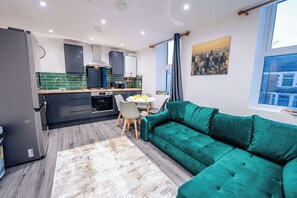 Eine moderne Küche mit Essbereich, einem grünen Sofa und Blick auf die Stadt.