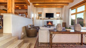 A spacious living room with a fireplace, comfortable seating, and a large TV. - Luxury Adobe Retreat with Jemez Mountain Views (Santa Fe)