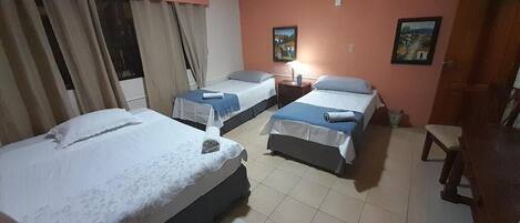 A hotel room with three beds, a nightstand, a chair, and two paintings on the wall.