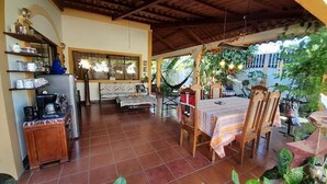 Een gezellig patio met een eettafel, stoelen en een hangmat. Er is een keuken met planken en een koelkast.
