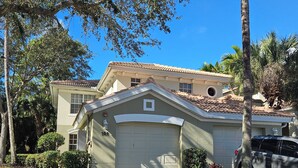 A residential house with a garage, a driveway, and surrounding greenery including trees and shrubs. - Cozy 2-bedroom condo with AC in fabulous Naples (Naples)