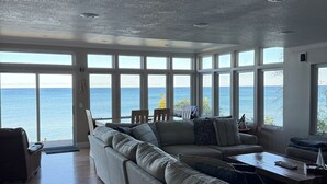 A spacious living room with a large sectional sofa, a coffee table, and a view of the sea through large windows. - Tranquil Lake Michigan 3-bedroom house perfect for a relaxing stay (Mears)