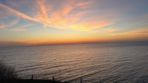 A sunset over a calm sea with a clear horizon and a few distant structures. - Tranquil Lake Michigan 3-bedroom house perfect for a relaxing stay (Mears)