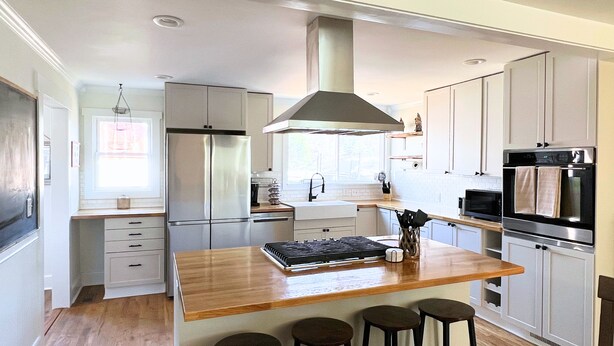 A modern kitchen with a central island, bar stools, stainless steel appliances, and a window providing natural light. - Historic 1890s Asheville Farmhouse Retreat • Sleeps 13 • Hot Tub + Playground (Asheville)