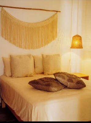 Ein Bett mit einer beigen Bettdecke, zwei Kissen und einer Wanddekoration aus Makramee.