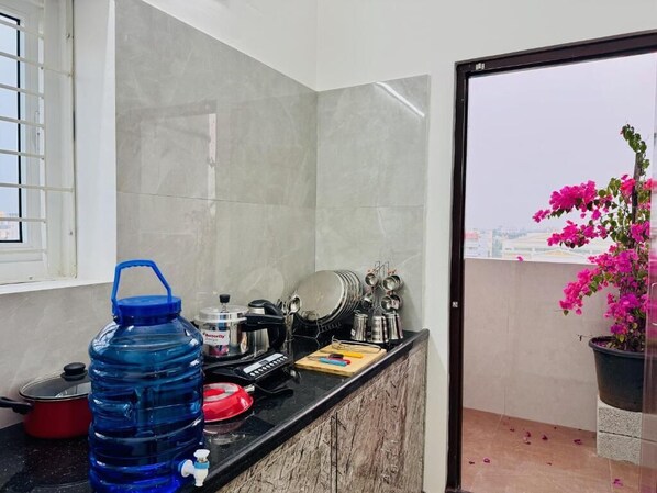 Una cocina con encimera de mármol, dispensador de agua azul, olla roja y planta en maceta con flores rosadas.