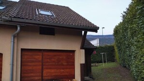 Una casa con techo de tejas, puerta de garaje de madera y una pila de leña afuera.