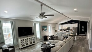 A spacious living area with a large sofa, a television, and a dining area with a kitchen in the background. - Beachview Bliss at The Billfish Luxury 4BR Home in Gulfport (Gulfport)