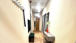 Un couloir avec un plancher en bois, un banc, un porte-manteau fixé au mur, une petite table avec un vase et une porte au fond.