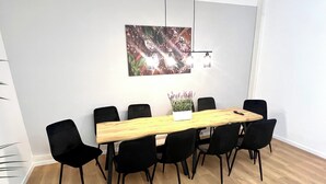 Une salle de conférence avec une table en bois, des chaises noires, un pot blanc contenant de la lavande et un luminaire suspendu.