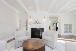 A modern living room with a fireplace, white sofas, and a round coffee table. - Luxury 5BR Home Minutes to Boston (Medford)