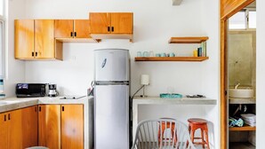 A compact kitchen with wooden cabinets, a stainless steel refrigerator, a microwave, and a coffee maker. There are two stools and a chair. - Cozy private studio apartment in Jaco with refreshing AC for your stay (Jaco)