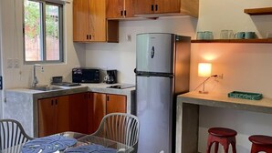 A compact kitchen with wooden cabinets, a stainless steel refrigerator, a microwave, a coffee maker, and a small dining area with a table and two chairs. - Cozy private studio apartment in Jaco with refreshing AC for your stay (Jaco)