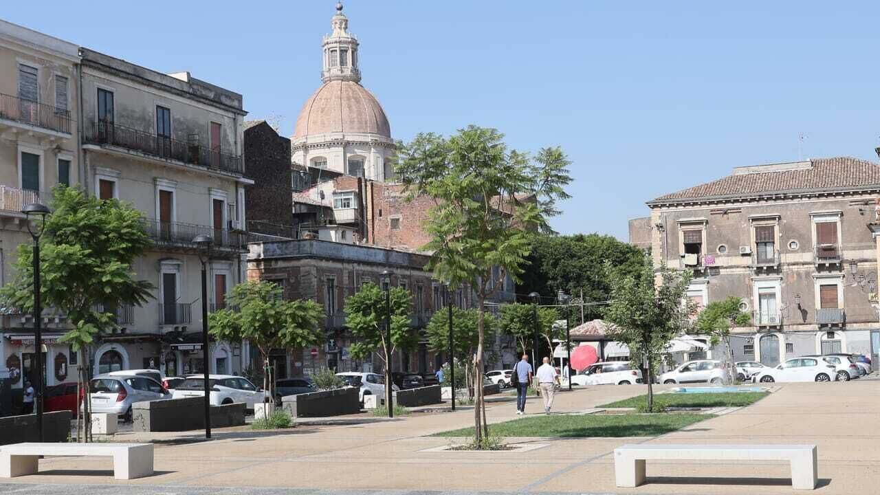 A square with a central monument, surrounded by trees and parked cars.