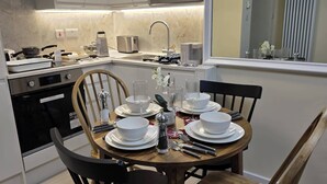 A modern kitchen with a dining table set for four, equipped with a stove, sink, and various kitchen appliances. - London Luxe Nest Your Perfect Short Stay (London)