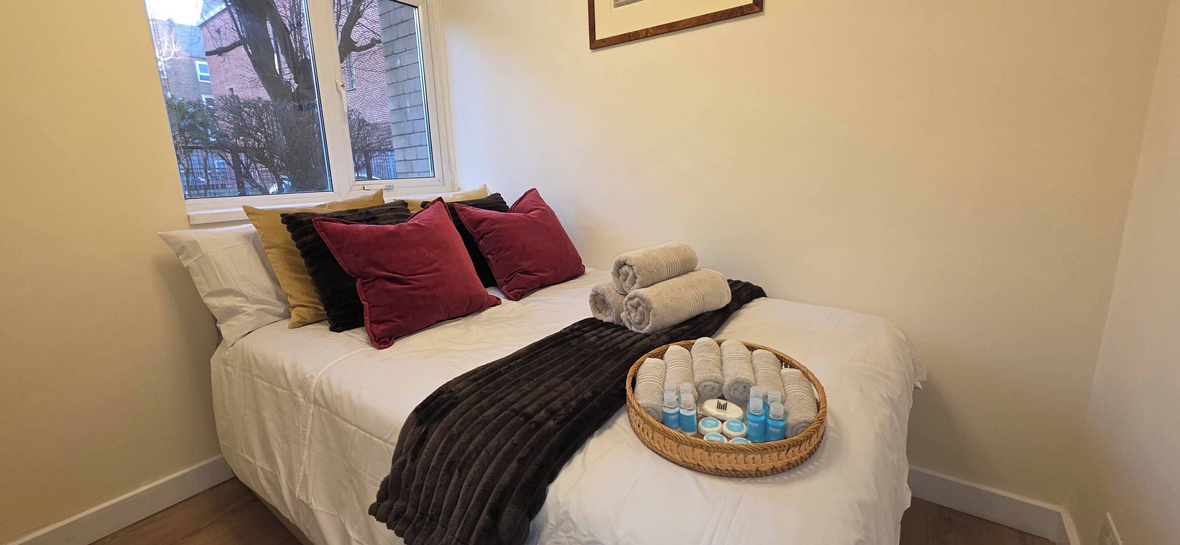 A neatly made bed with pillows, a blanket, and a basket of toiletries.
