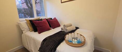 A neatly made bed with pillows, a blanket, and a basket of toiletries.