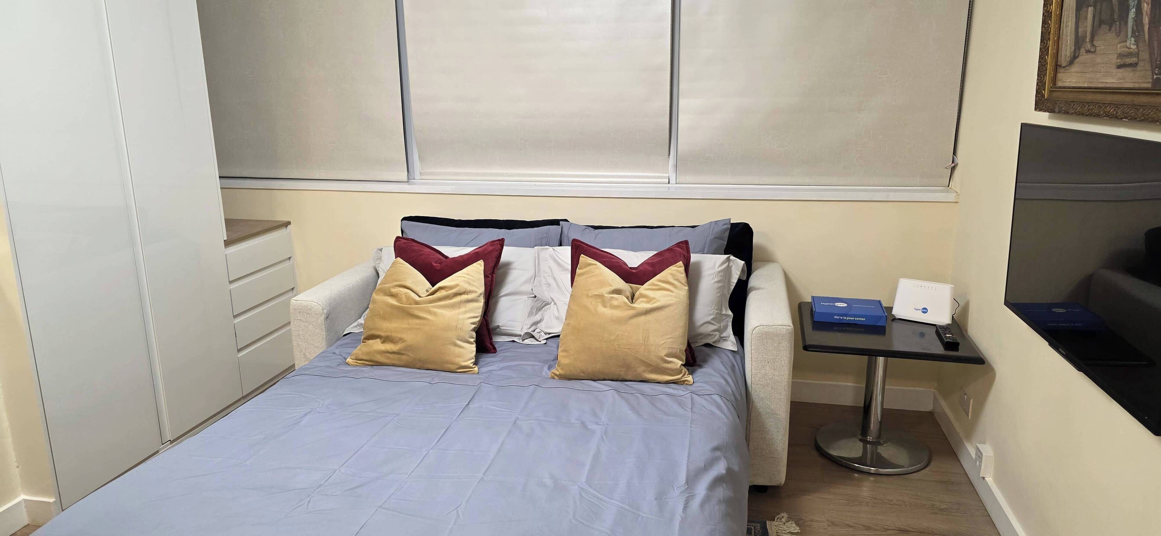 Een slaapkamer met een bed, nachtkastje, bureau en raam met zonwering.