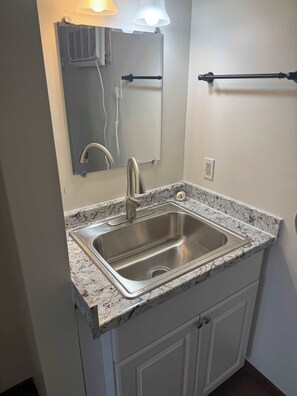 A bathroom with a stainless steel sink, a mirror, and a towel rack. - Stand Rock Studios in Wisconsin Dells! (Unfurnished) (Wisconsin Dells)