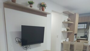 Ein modernes Wohnzimmer mit einem Wand-Fernseher, einer Holz-Unterhaltungseinrichtung darunter und einem Essbereich mit Tisch und Stühlen.