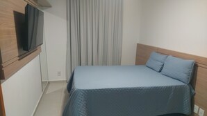 Ein Schlafzimmer mit einem Bett, einem Fernseher auf einer Holzkommode und einem Fenster mit Vorhängen.