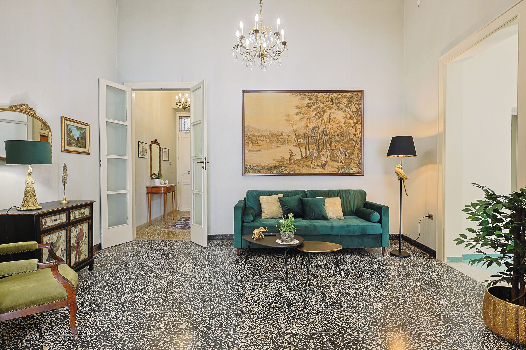 Una stanza con un divano verde, un lampadario, un quadro di grandi dimensioni e una pianta in vaso.