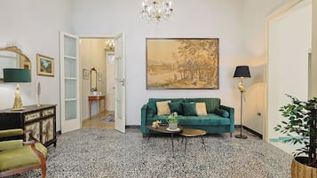 Una stanza con un divano verde, un lampadario, un quadro di grandi dimensioni e una pianta in vaso.