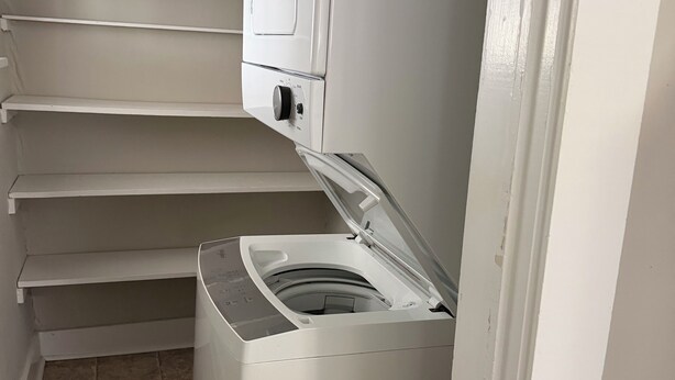 A laundry room with a front-loading washer and dryer, a tiled floor, and a vent.