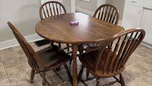 A dining area with a round wooden table surrounded by four chairs, a window with blinds, and a white cabinet.