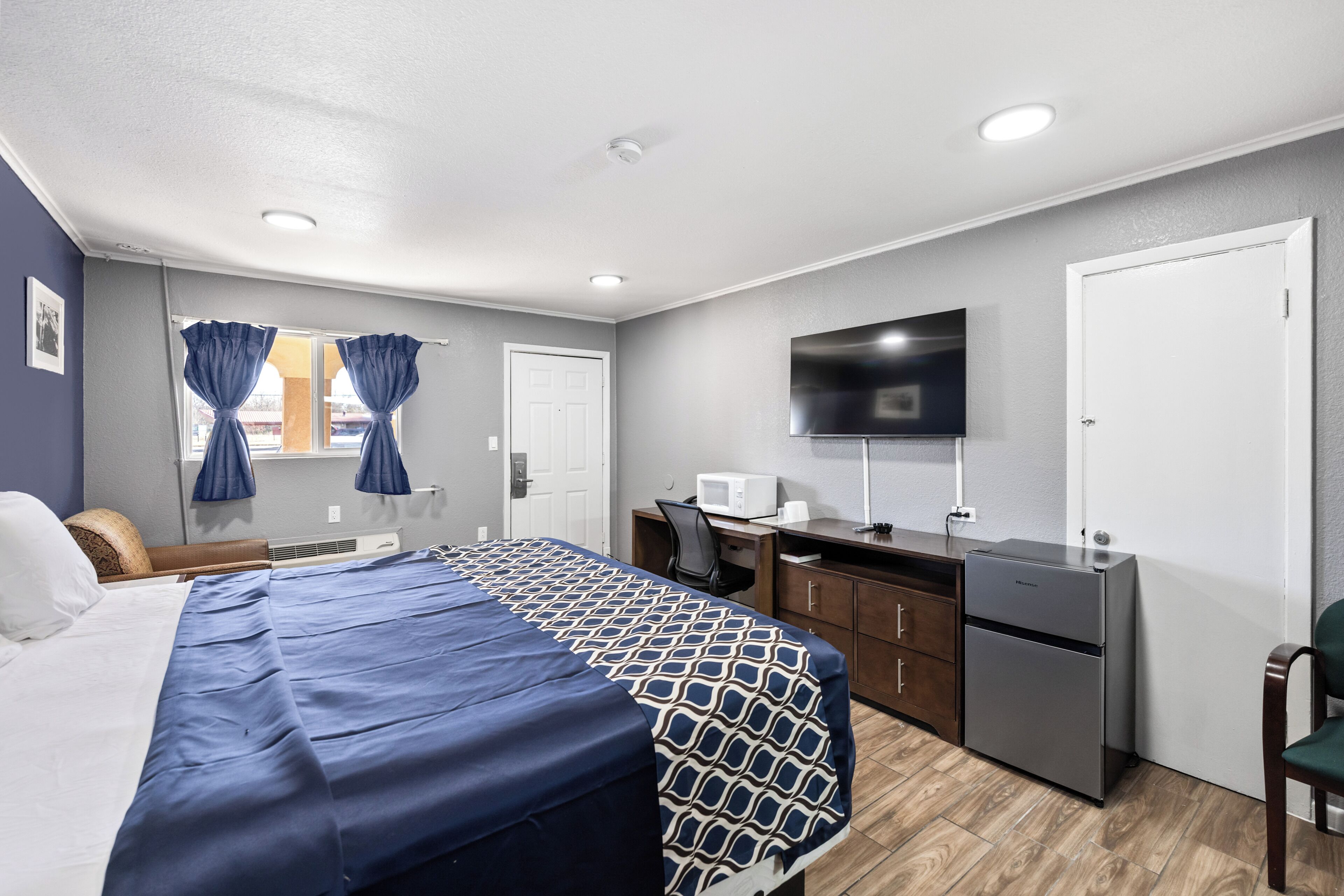 A hotel room with a bed, desk, chair, television, and a refrigerator.