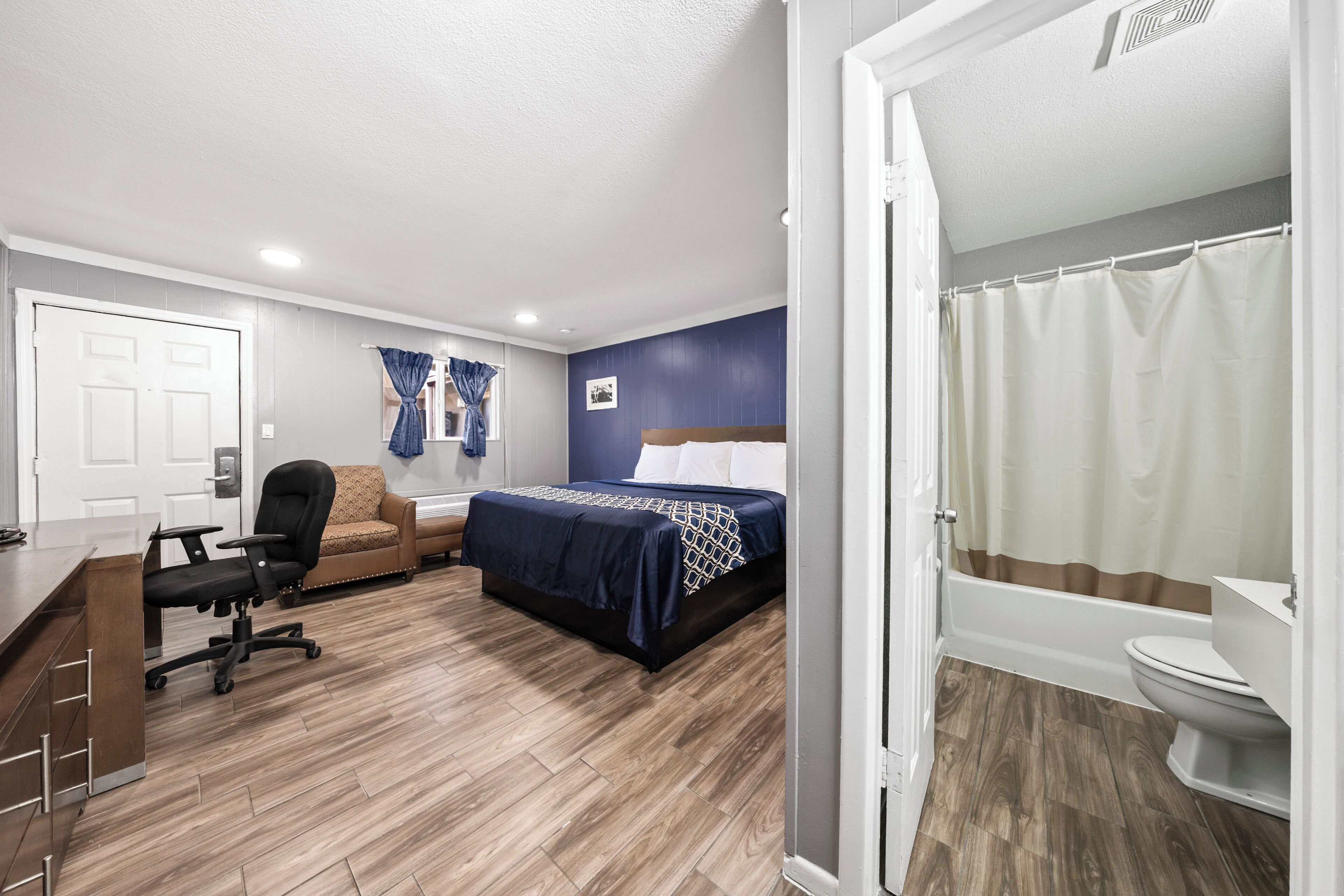 Un dormitorio con cama, escritorio, silla, sofá y baño con inodoro y cortina de ducha.