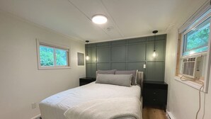 Une chambre à coucher comprenant un lit, des tables de chevet, une fenêtre et un appareil de climatisation.